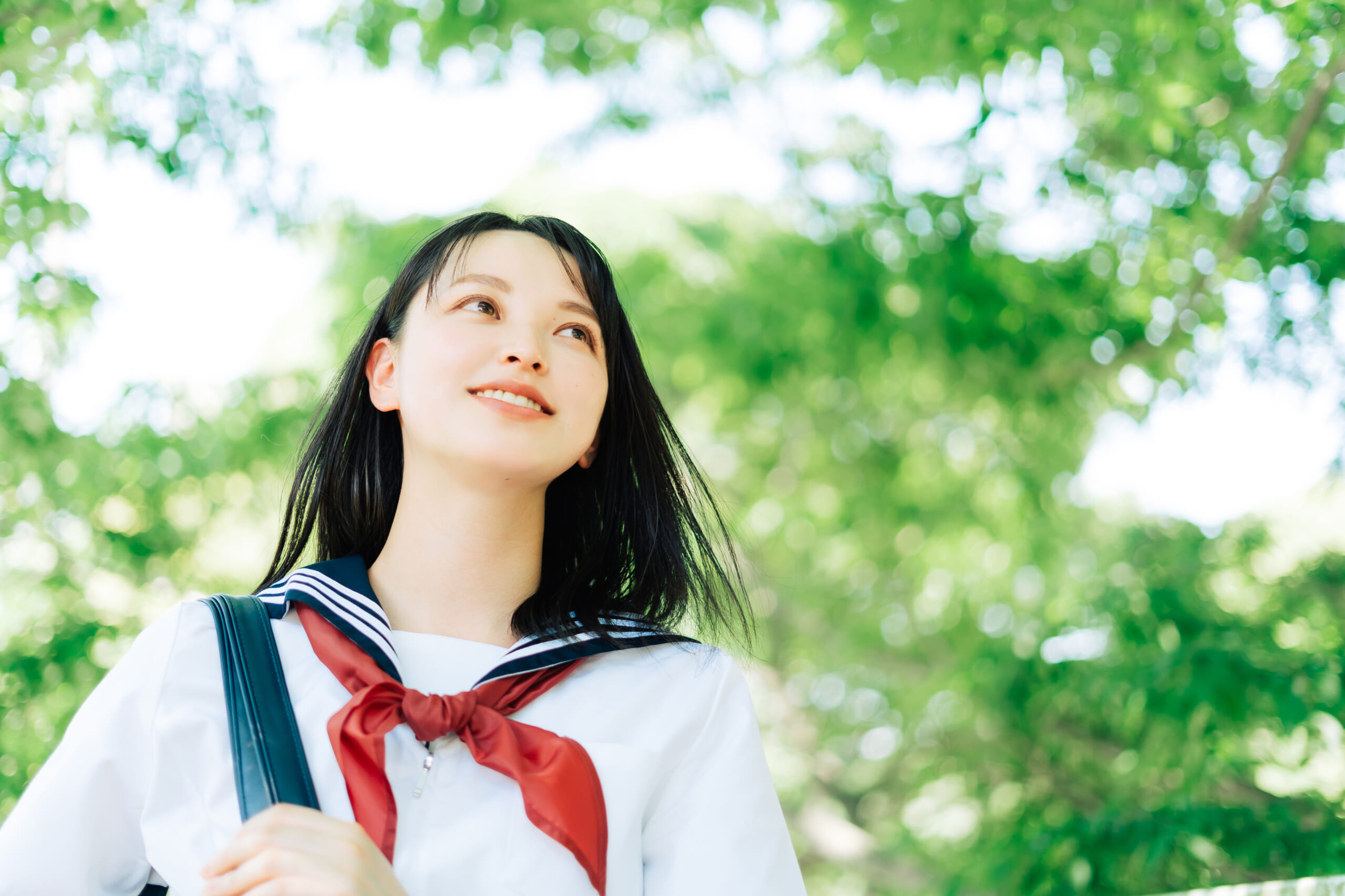 前を向く女学生の写真、背景には新緑に囲まれた青空